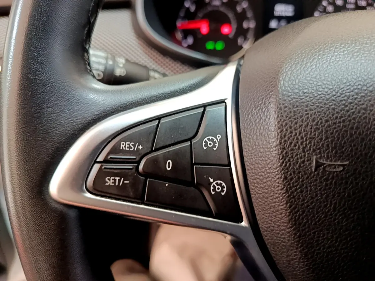 Gros plan sur les commandes du régulateur de vitesse au volant cuir de la Dacia Sandero Confort blanche 2022.