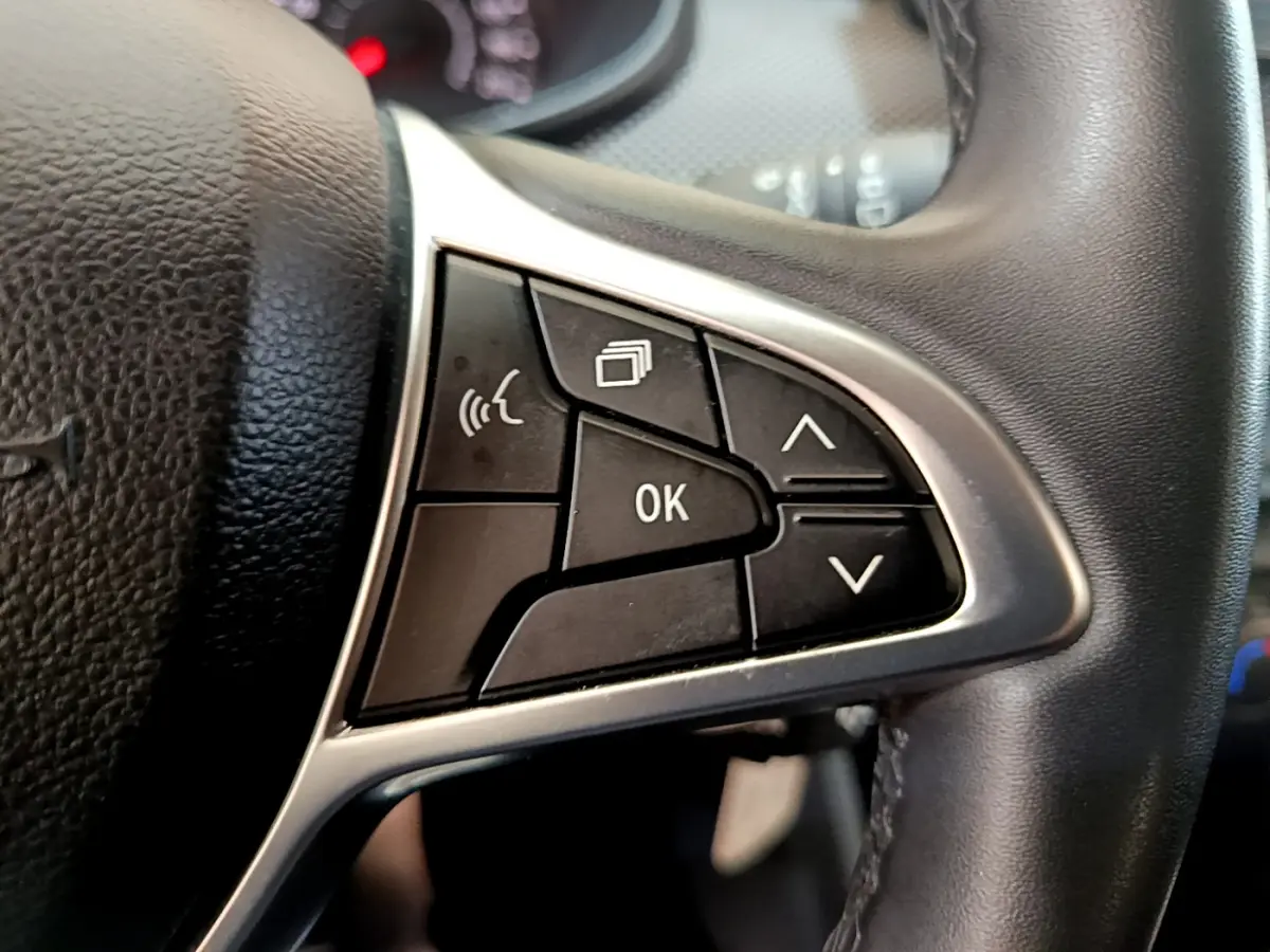 Gros plan sur les commandes multifonctions côté gauche du volant cuir noir de la Dacia Sandero Confort TCe 90 blanche 2022.