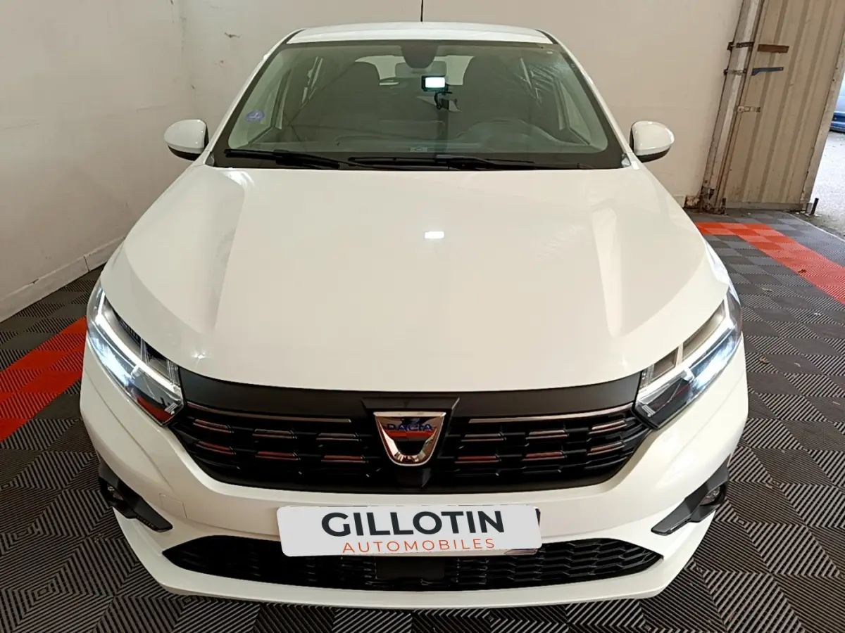 Vue frontale d'une Dacia Sandero Confort TCe 90 blanche avec calandre noire et phares LED allumés.