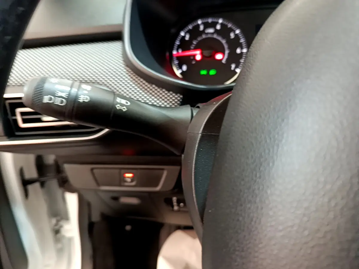 Gros plan sur la manette de clignotant à gauche du volant cuir d'une Dacia Sandero blanche, tableau de bord en arrière-plan.