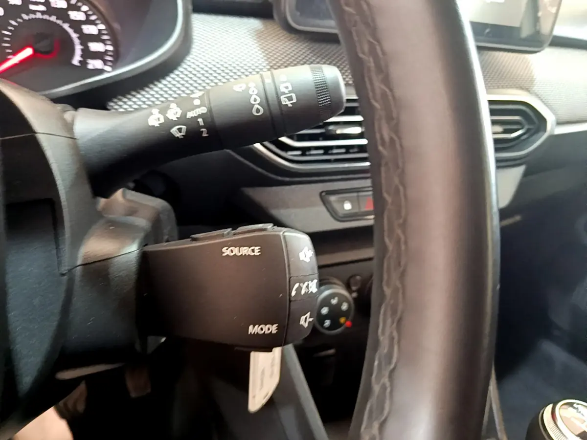 Gros plan sur le volant cuir et commandes multimédia à gauche du tableau de bord d'une Dacia Sandero blanche 2022.