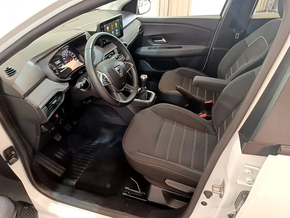 Intérieur de la Dacia Sandero blanc vue côté conducteur, tableau de bord moderne avec écran tactile et volant cuir.