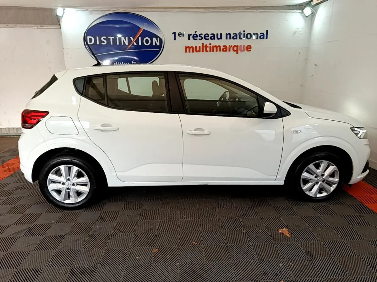 Profil droit d'une Dacia Sandero Confort TCe 90 blanche 2022, stationnée en intérieur sur sol noir et rouge.