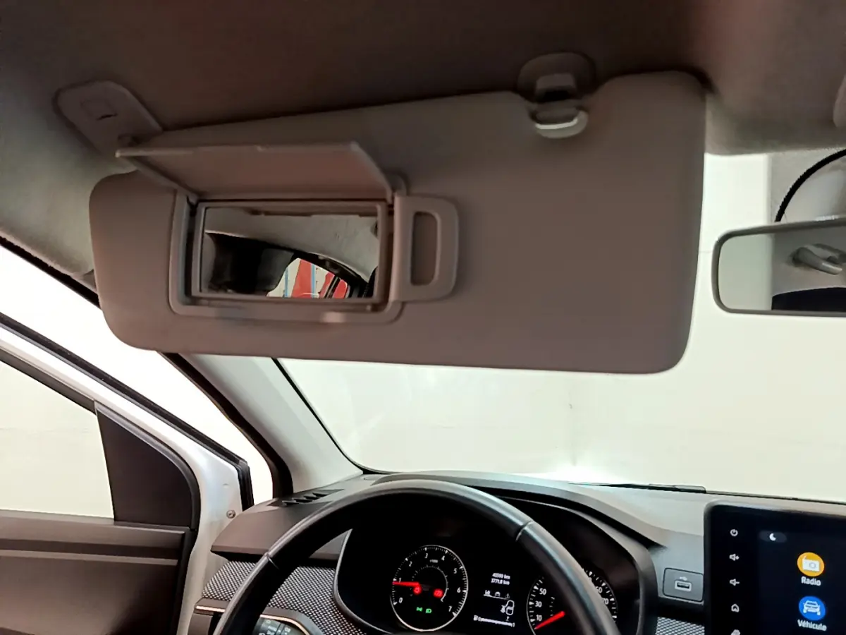 Vue intérieure du tableau de bord et volant cuir noir d'une Dacia Sandero blanche, avec pare-soleil et miroir ouvert.