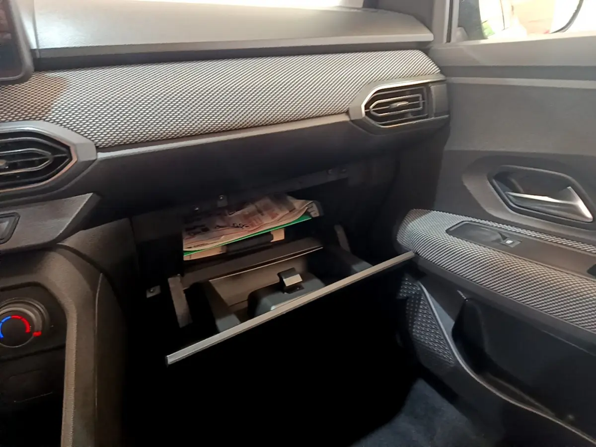 Intérieur côté passager d'une Dacia Sandero blanc 2022, boîte à gants ouverte avec documents visibles.