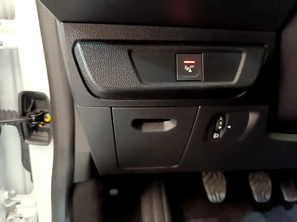 Vue rapprochée du tableau de bord côté gauche d'une Dacia Sandero blanc 2022, avec bouton désactivation capteurs de stationnement.