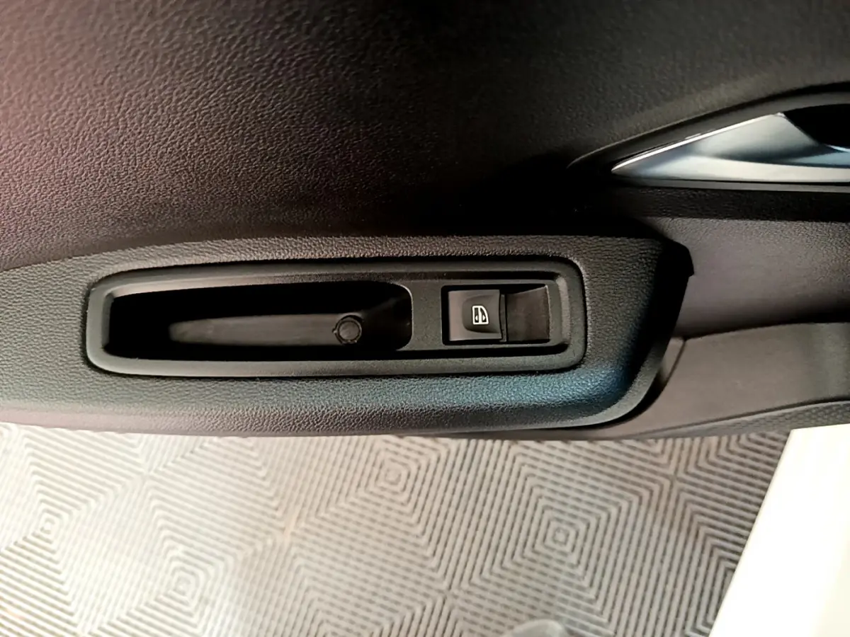 Gros plan sur la poignée intérieure noire et l'interrupteur de lève-vitre côté conducteur d'une Dacia Sandero blanche.