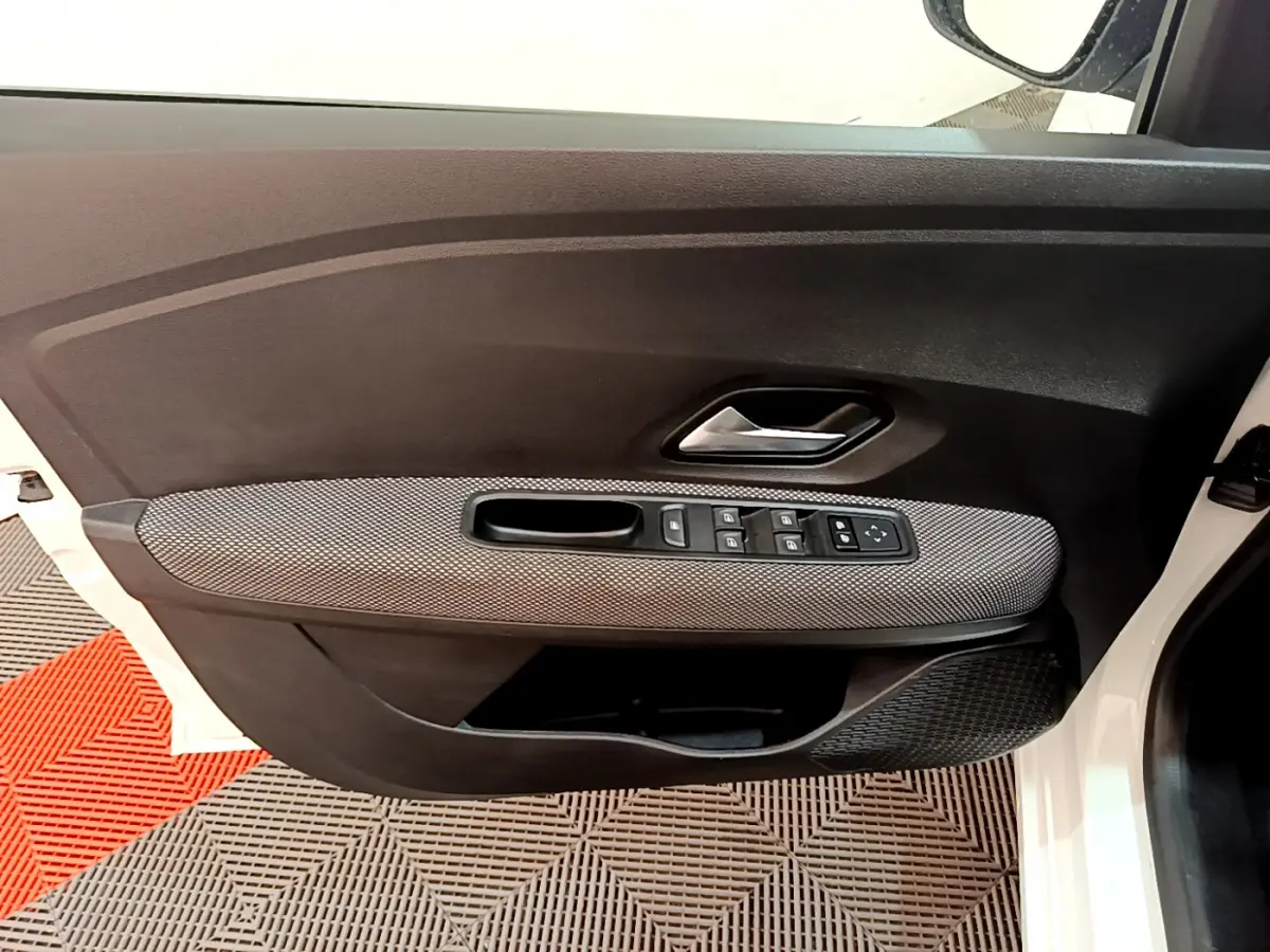 Vue intérieure côté gauche de la porte avant blanche de la Dacia Sandero Confort TCe 90 avec commandes de vitres et poignée chrome.