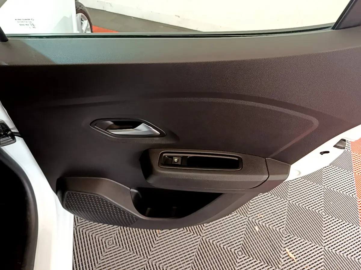 Détail de la porte intérieure côté gauche d'une Dacia Sandero blanche, avec poignée et commande de vitre électrique.