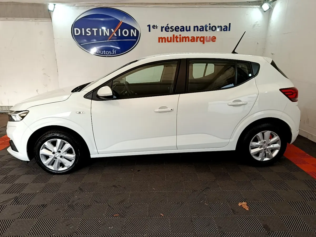 Profil côté gauche d'une Dacia Sandero Confort TCe 90 blanche de 2022, stationnée en intérieur sur sol à damiers.