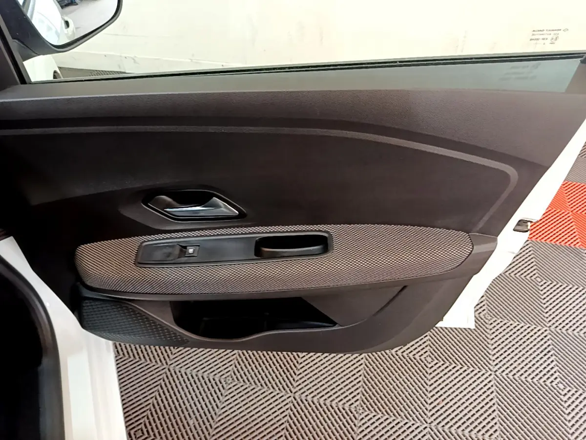 Vue intérieure de la porte avant gauche blanche d'une Dacia Sandero Confort TCe 90 avec poignée et commande de vitre.