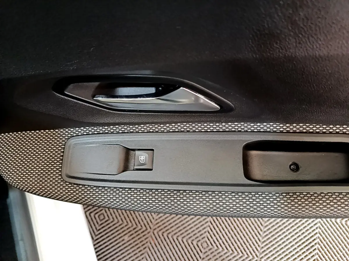 Gros plan sur la poignée intérieure et le bouton de lève-vitre côté gauche de la porte d'une Dacia Sandero blanche.