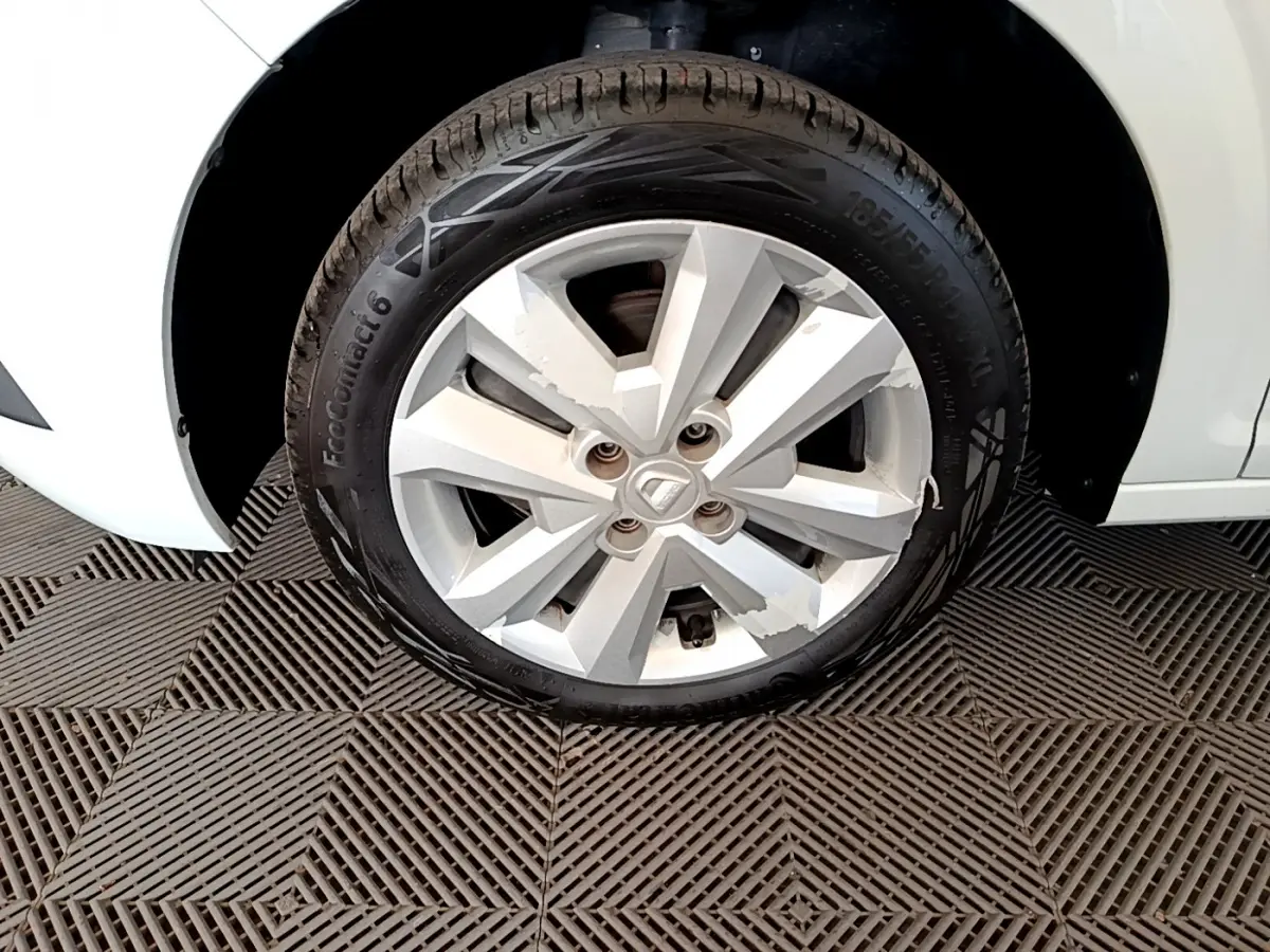 Gros plan sur la roue avant gauche d'une Dacia Sandero blanche, jante alliage avec logo central visible.