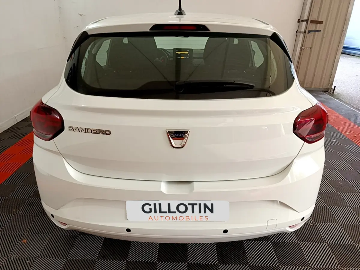 Vue arrière d'une Dacia Sandero blanche 2022 avec feux rouges et logo centré sur un sol à damiers noir et rouge.