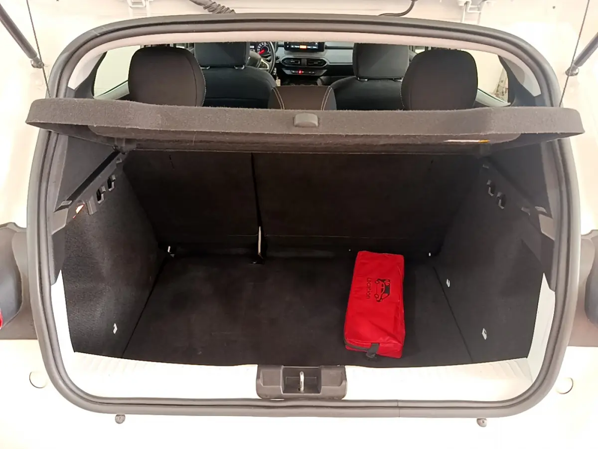 Coffre ouvert d'une Dacia Sandero blanche 2022, montrant l'intérieur noir avec une trousse de secours rouge.
