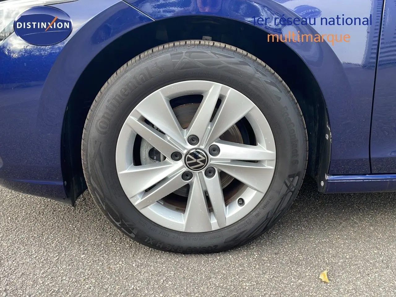 Gros plan sur la roue avant gauche d'une Volkswagen Golf VIII bleu lapiz metal avec jante alliage cinq branches.