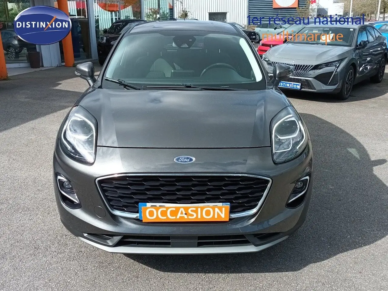 Vue avant d'une Ford Puma gris foncé métal avec calandre noire et plaque "OCCASION" orange visible.