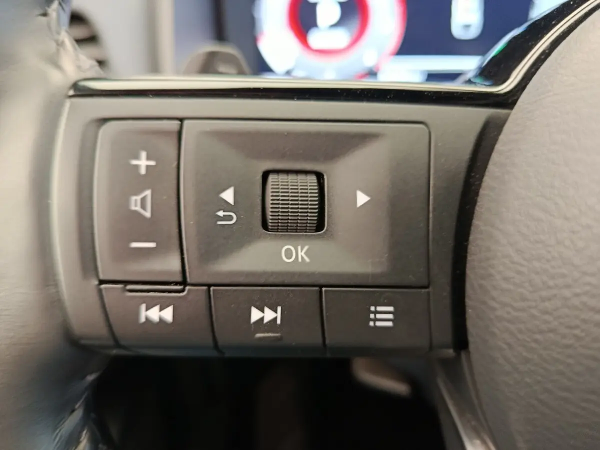 Gros plan sur les commandes multifonctions noires du volant du Nissan Qashqai 2023, avec boutons de réglage et navigation.