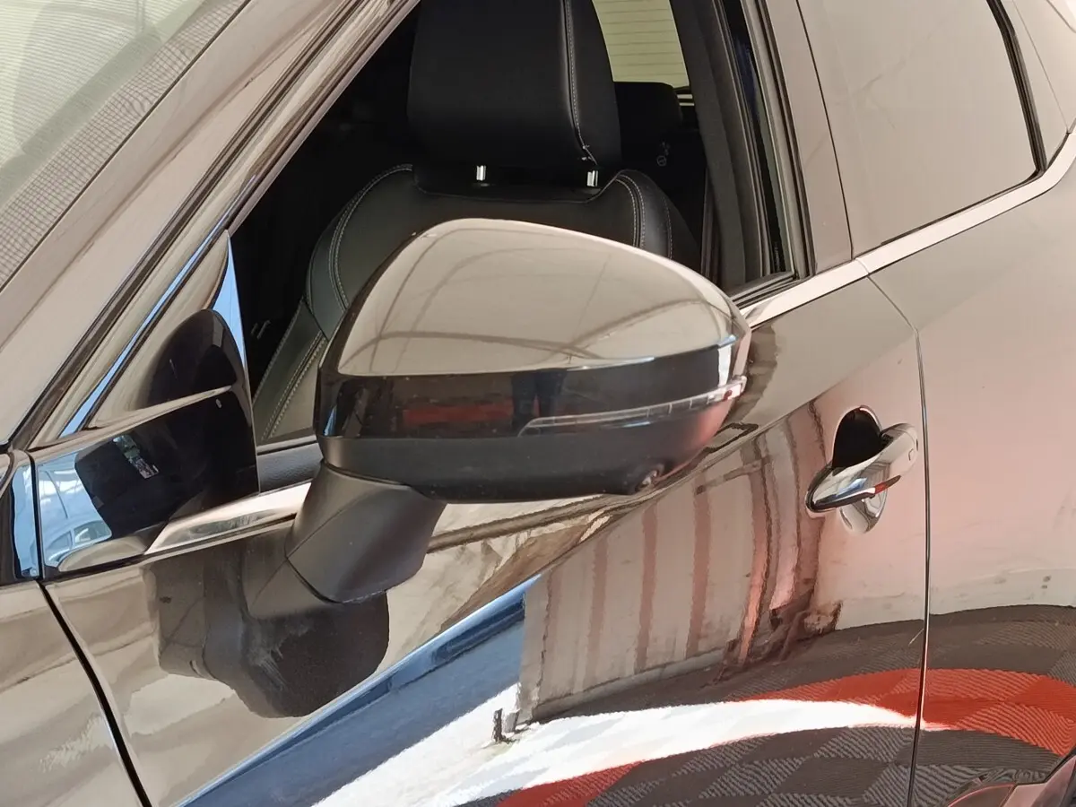 Rétroviseur côté conducteur noir brillant sur Nissan Qashqai 2023, vue rapprochée du côté gauche avec porte et poignée visibles.