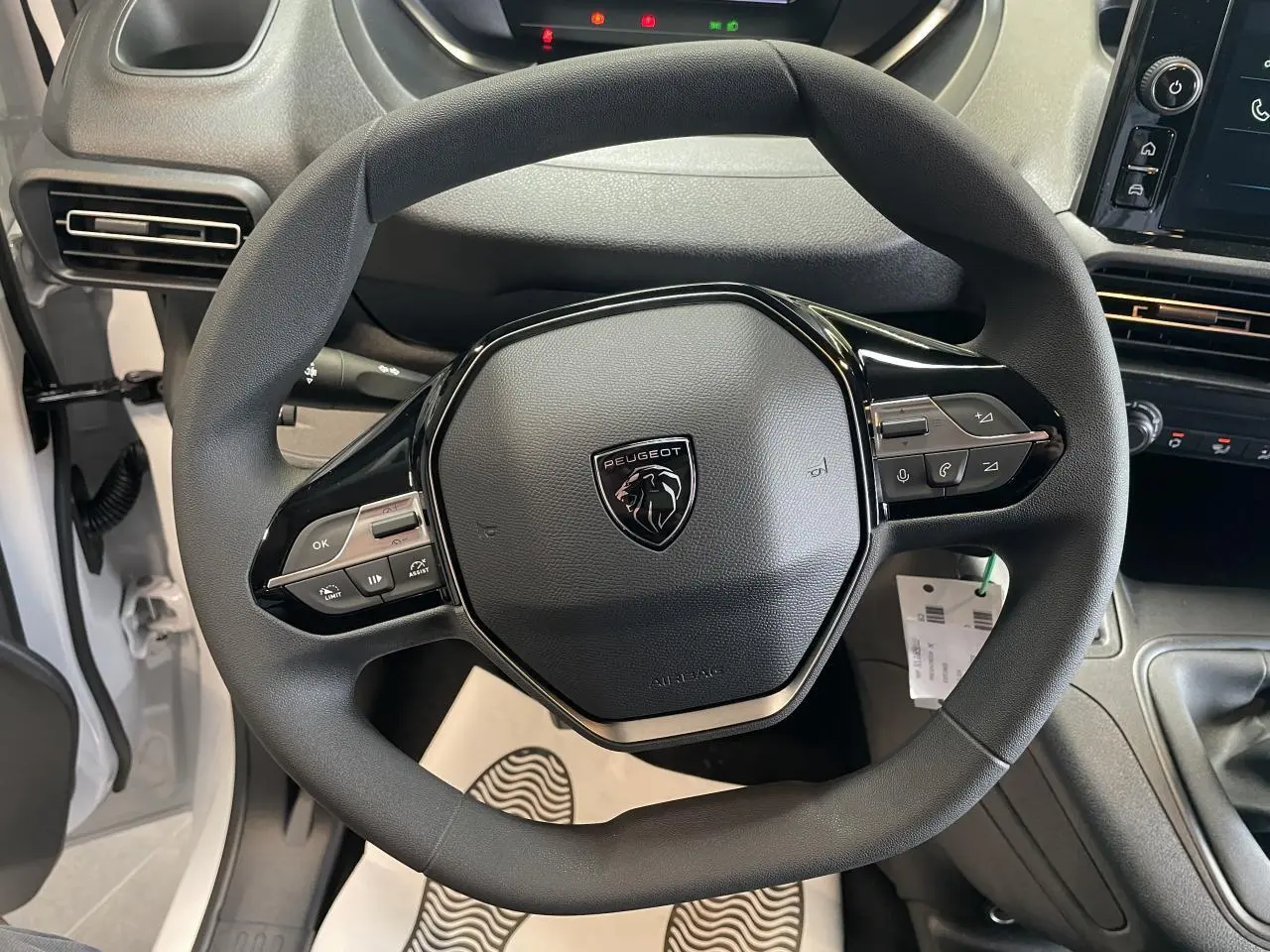 Vue rapprochée du volant multifonctions noir de la Peugeot Partner blanche, avec tableau de bord et levier de vitesses visibles.