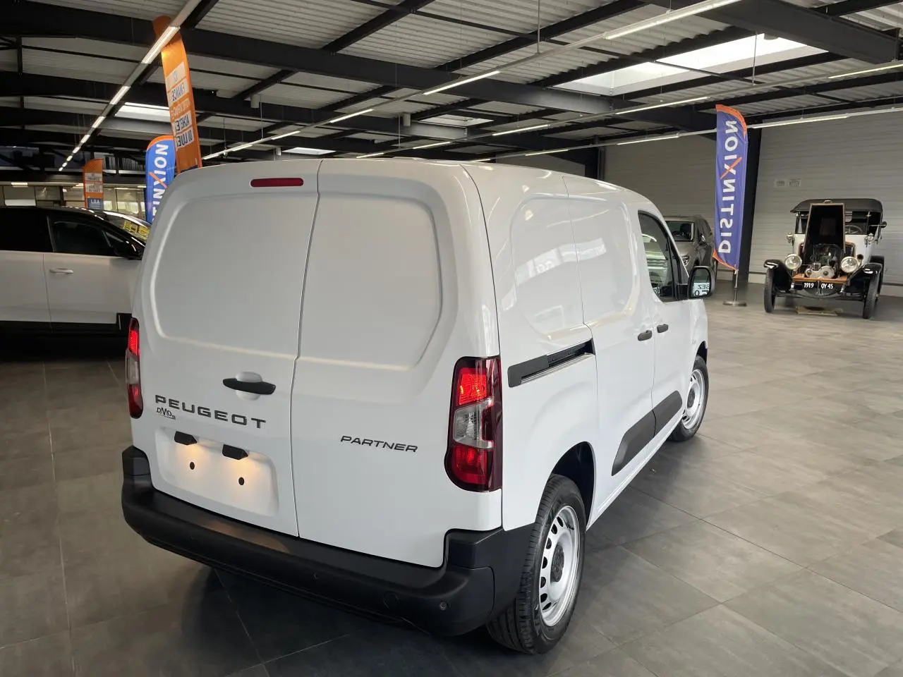 Vue 3/4 arrière droite du Peugeot Partner blanc, fourgon utilitaire en intérieur avec portes arrière battantes fermées.