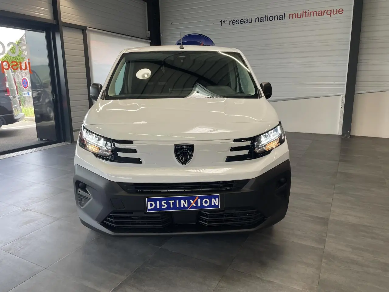 Vue frontale d’un utilitaire Peugeot Partner blanc avec calandre noire et logo lion au centre, en intérieur showroom.