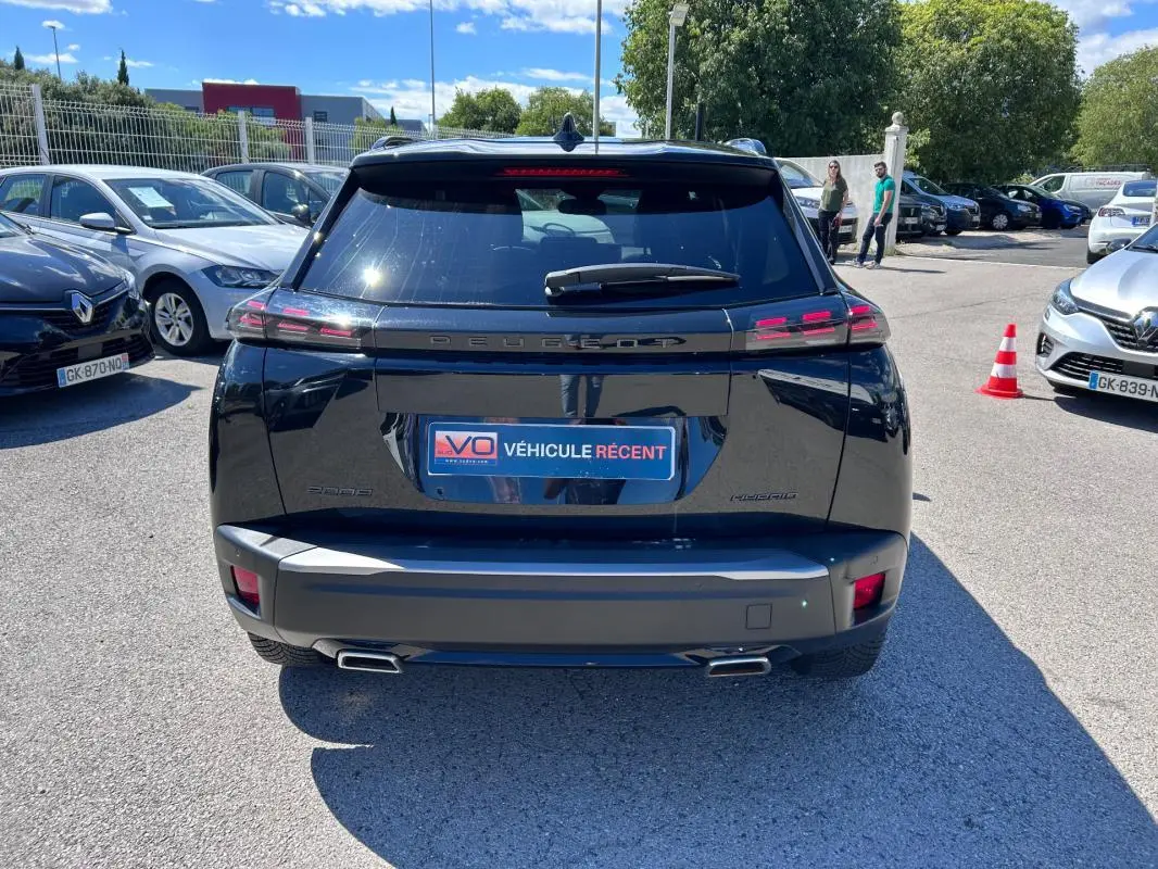 Vue arrière d’un Peugeot 2008 Hybrid noir 2025 avec barres de toit et double sortie d’échappement visible en extérieur.
