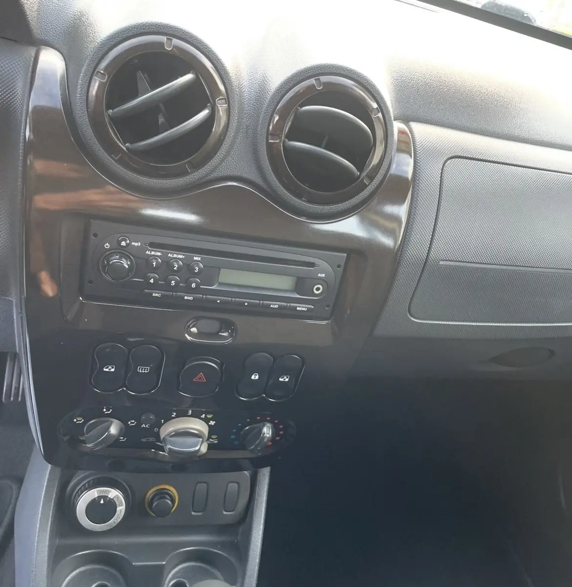 Intérieur du tableau de bord gris foncé du Dacia Duster 2011, avec commandes de climatisation et levier de vitesses manuel visible.