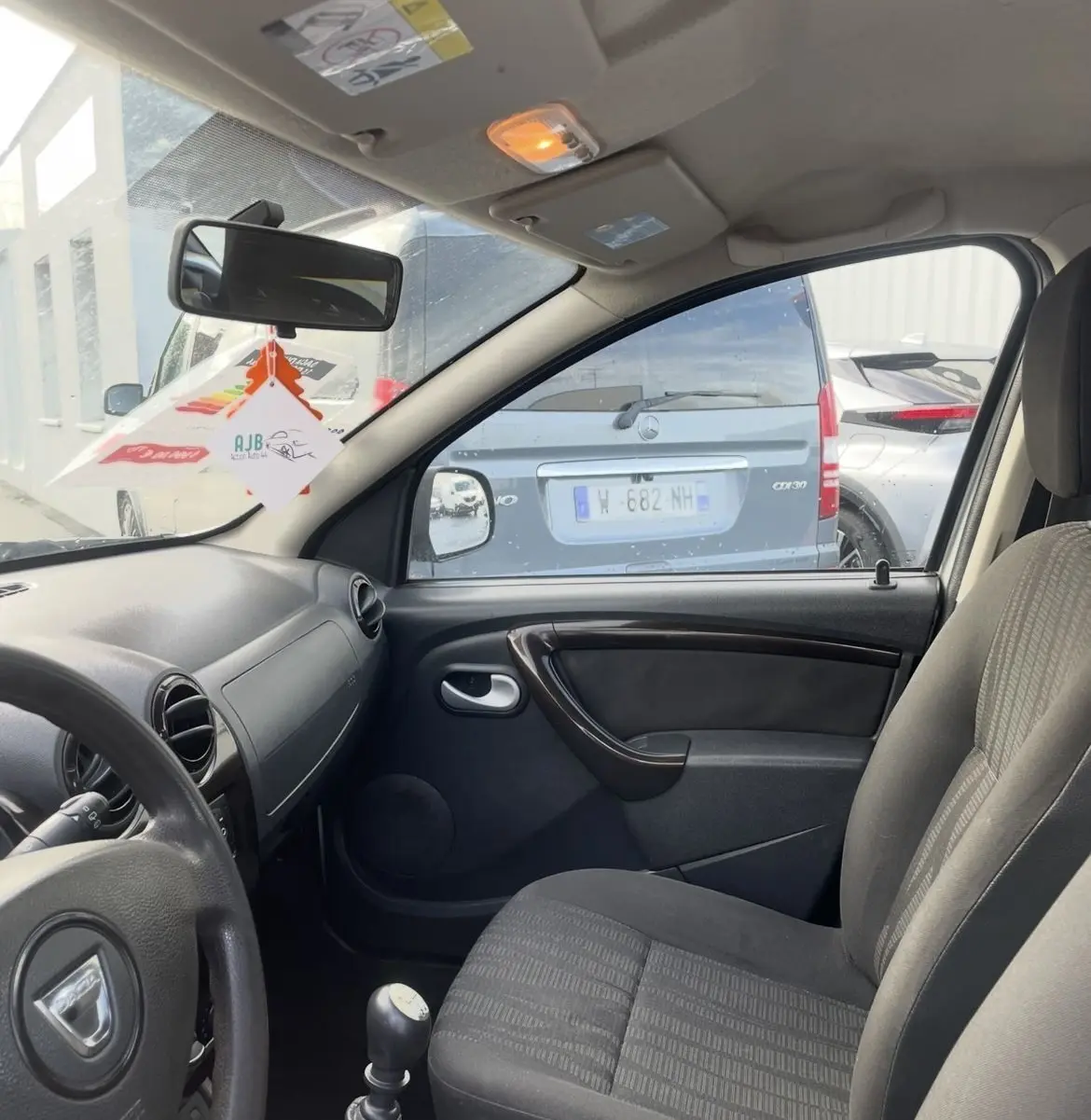 Vue intérieure côté conducteur du Dacia Duster 2011, montrant le volant, levier de vitesse manuel et siège tissu gris.