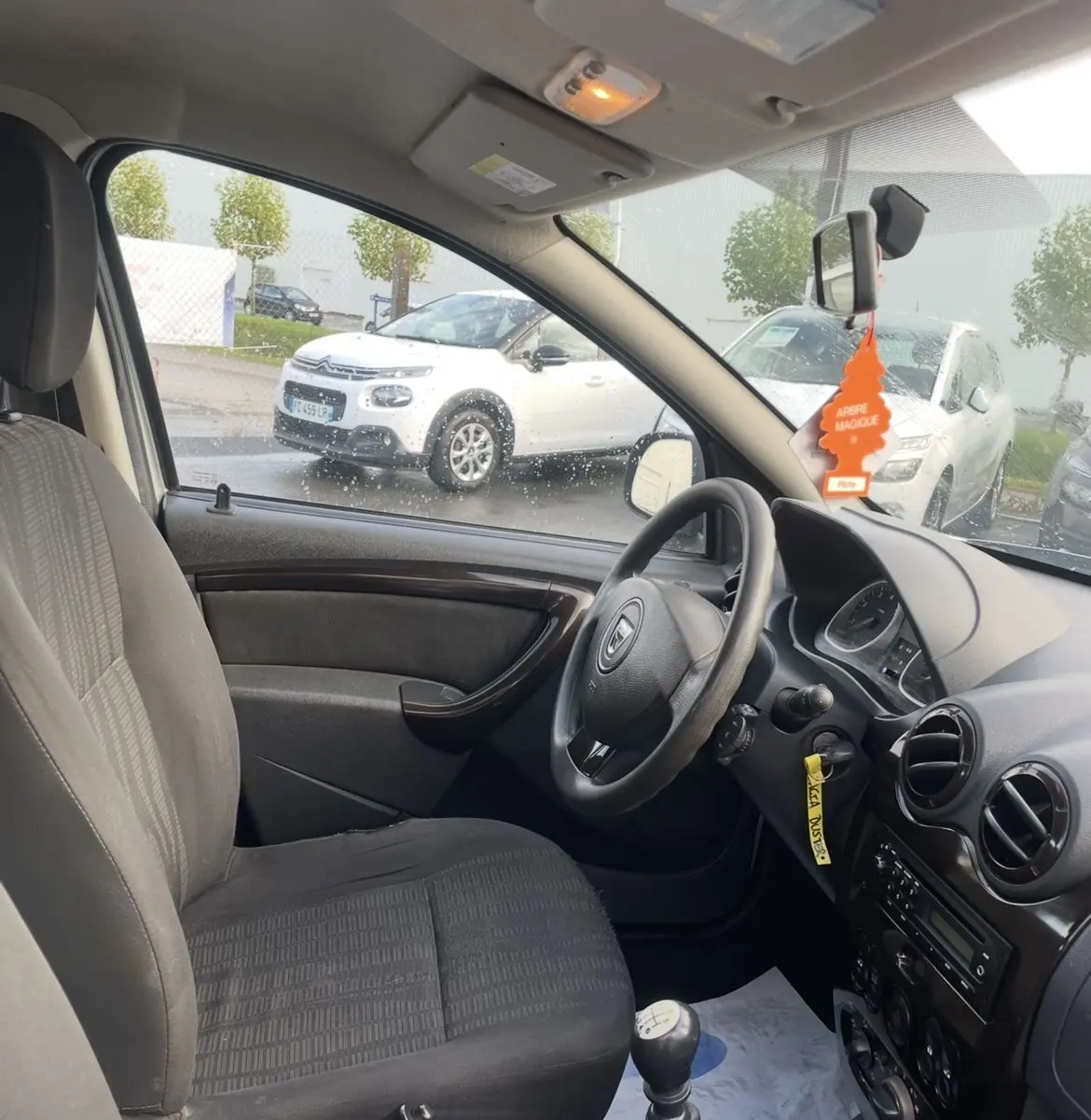 Vue intérieure côté conducteur du Dacia Duster gris 2011 avec volant, levier de vitesse manuel et tableau de bord visible.