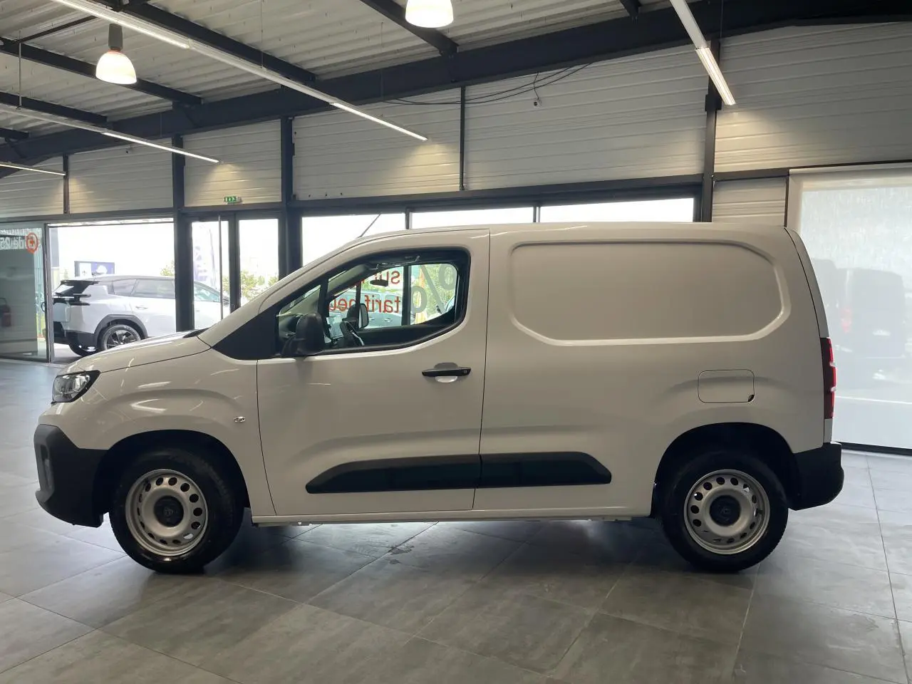 Vue de profil côté gauche d’un Peugeot Partner blanc en fourgon, avec jantes tôles grises et protections noires sur les portières.