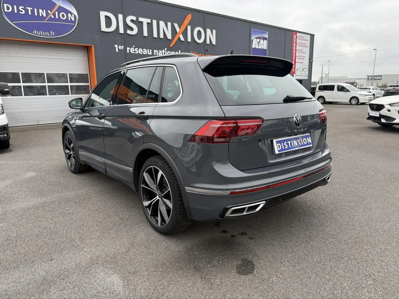 Vue 3/4 arrière droite d'un Volkswagen Tiguan gris dauphin avec jantes alliage 20 pouces sur parking extérieur.