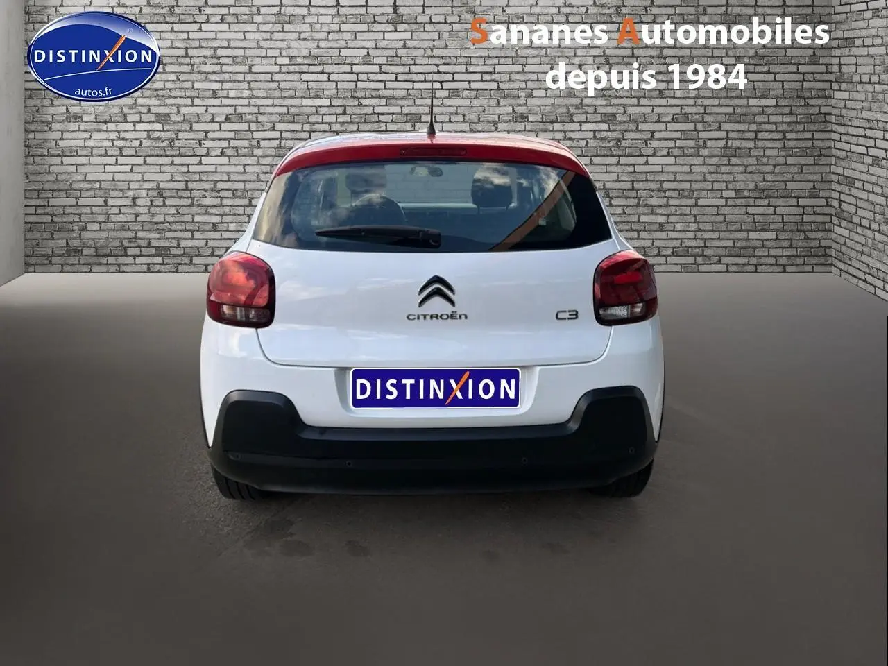 Vue arrière d'une Citroën C3 blanche de 2018 avec feux rouges et pare-chocs noir mat dans un décor urbain.