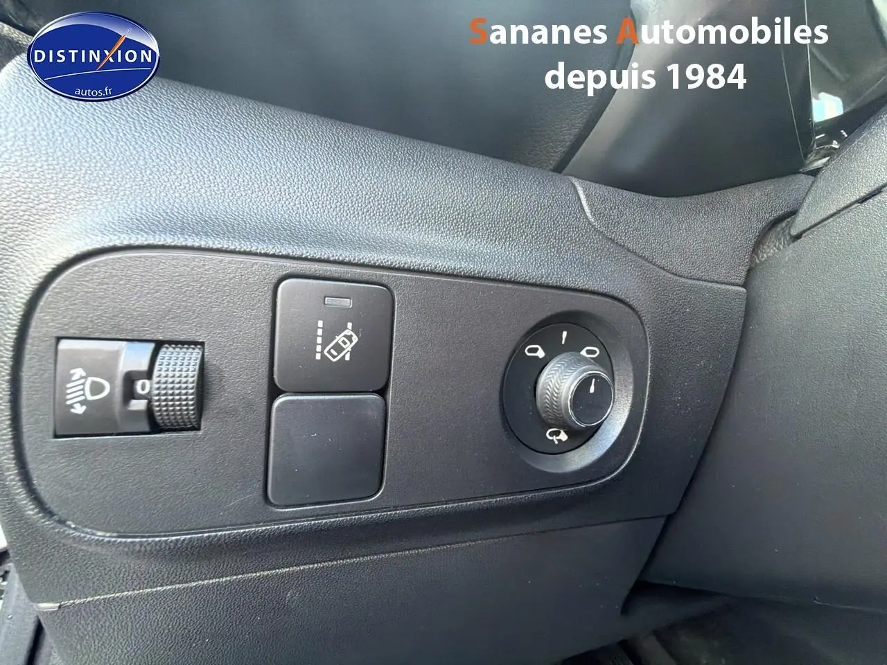 Gros plan sur les commandes de réglage des rétroviseurs et des phares à gauche du volant dans une Citroën C3 blanche 2018.