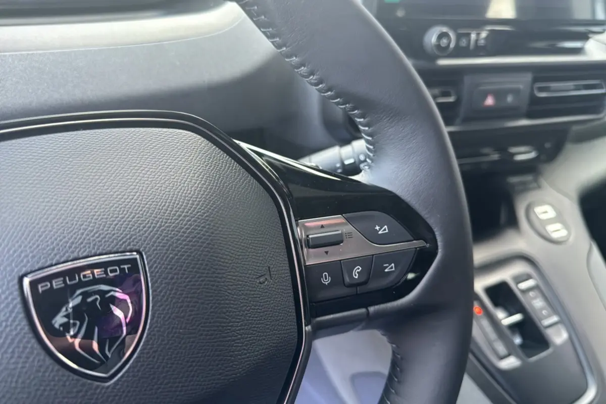 Gros plan sur le volant cuir multifonctions du Peugeot Rifter 2026 avec logo lion et commandes intégrées.