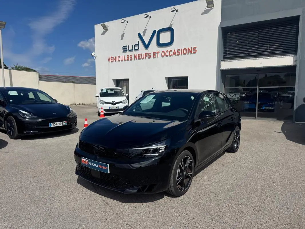Opel Corsa 1.2 Turbo Hybrid noir vue 3/4 avant droit avec jantes alliage 17 pouces, stationnée devant un garage.