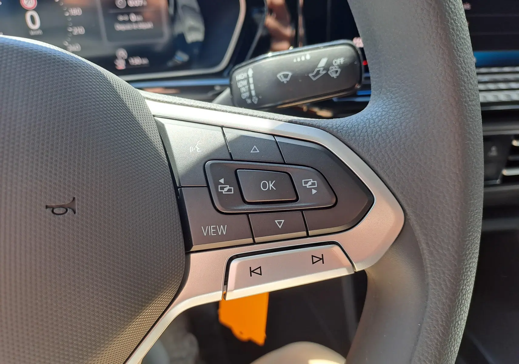 Gros plan sur les commandes multifonctions à droite du volant du Volkswagen Caddy Cargo Maxi blanc, tableau de bord en arrière-plan.