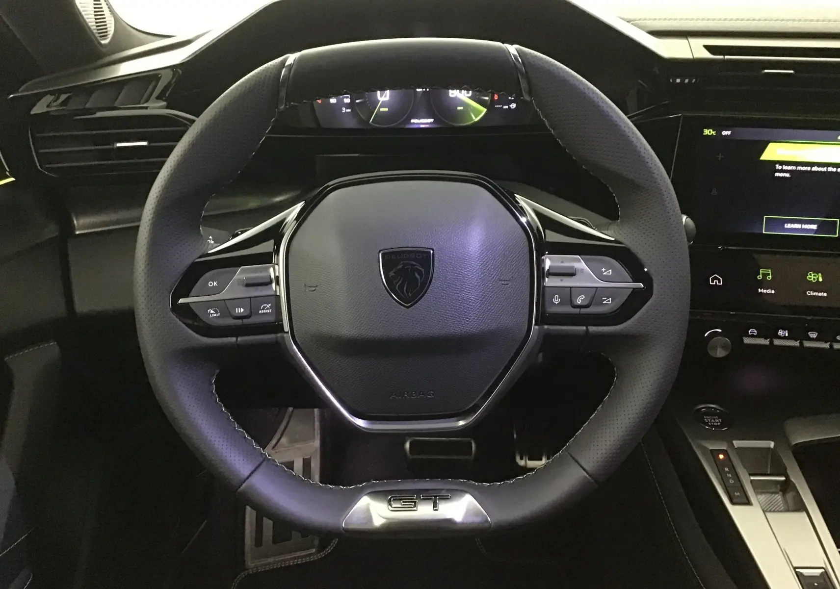 Volant cuir noir GT de la Peugeot 308 2025 avec commandes intégrées et tableau de bord numérique en arrière-plan.