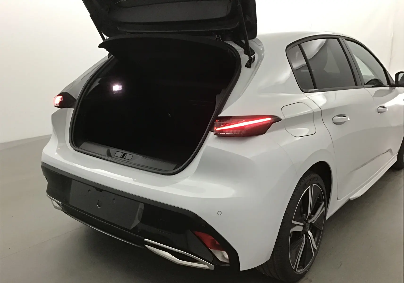 Vue 3/4 arrière droite d'une Peugeot 308 blanche Okenite avec coffre ouvert et feux arrière allumés.