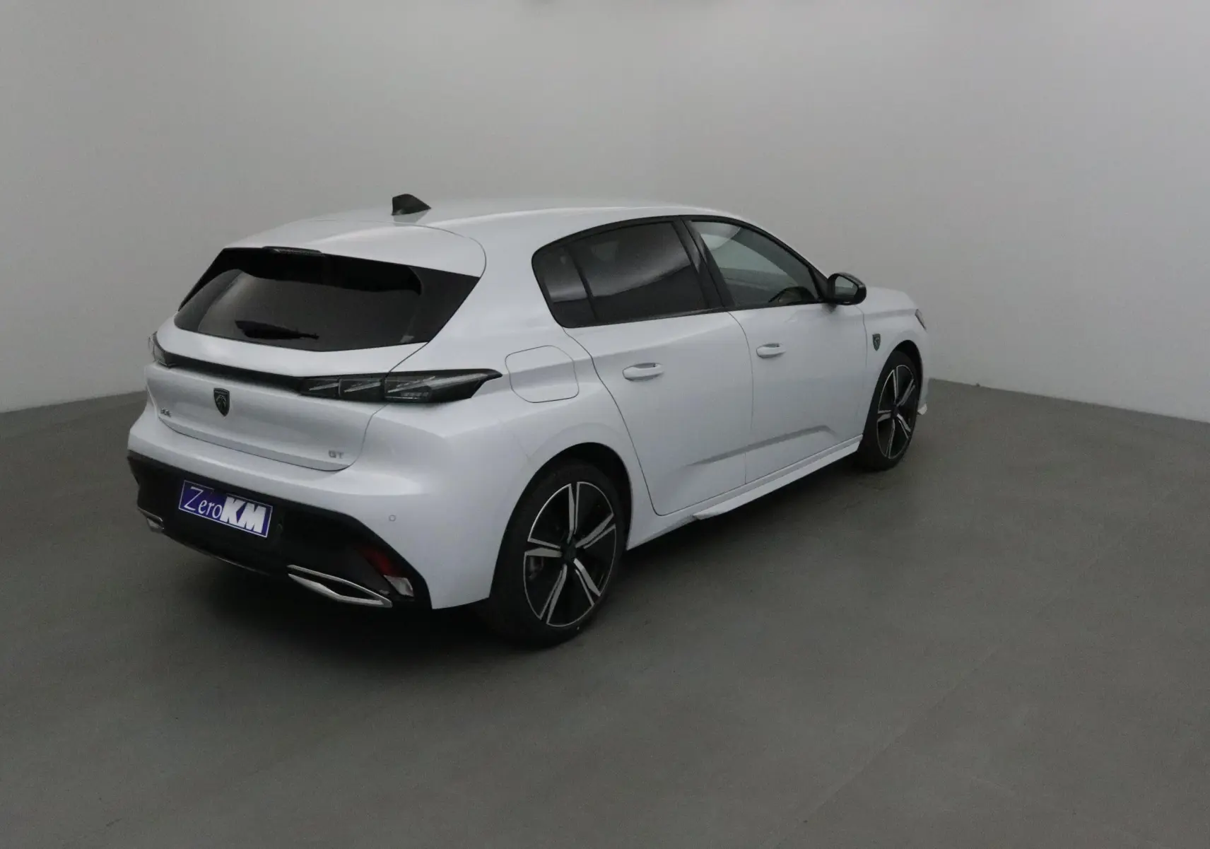 Peugeot 308 GT blanc Okenite vue 3/4 arrière droit dans un studio, avec jantes alliage et vitres teintées.