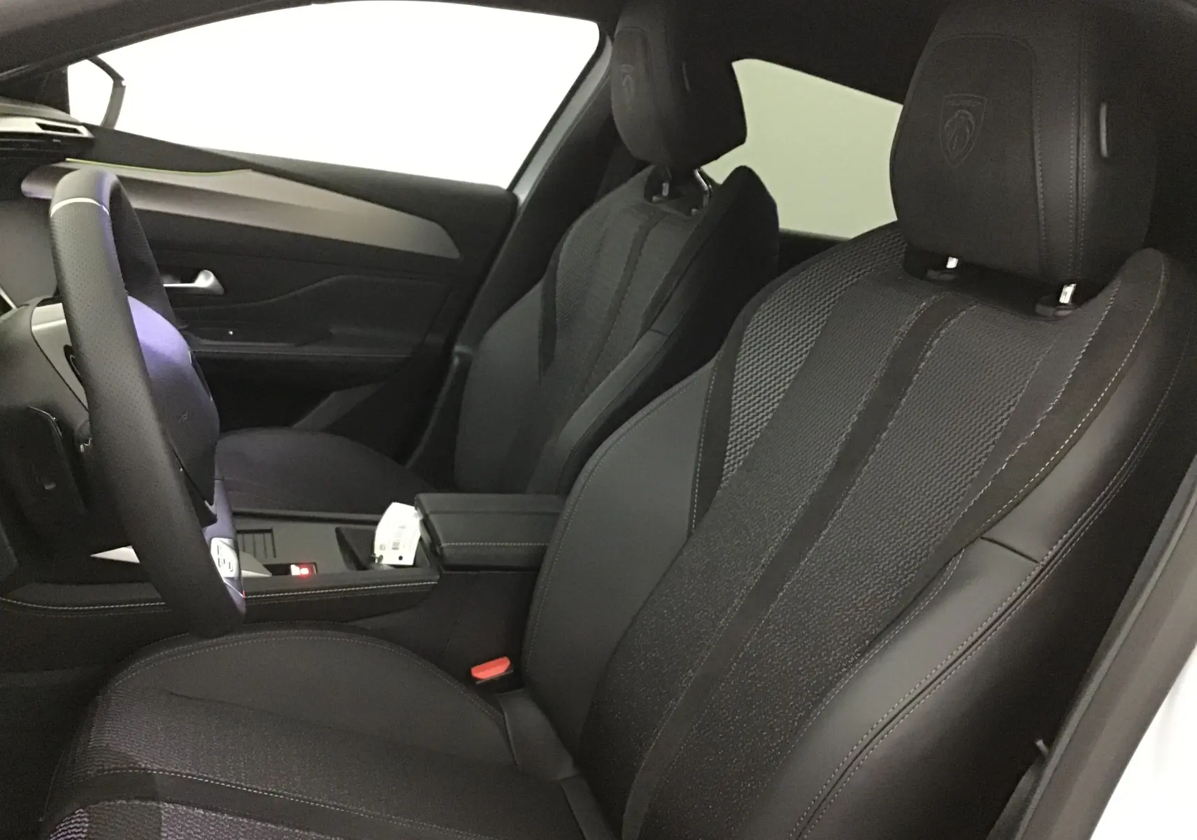 Intérieur avant de la Peugeot 308 GT+Pack Alcantara 2025, sièges noirs en cuir et Alcantara avec logo Peugeot brodé.