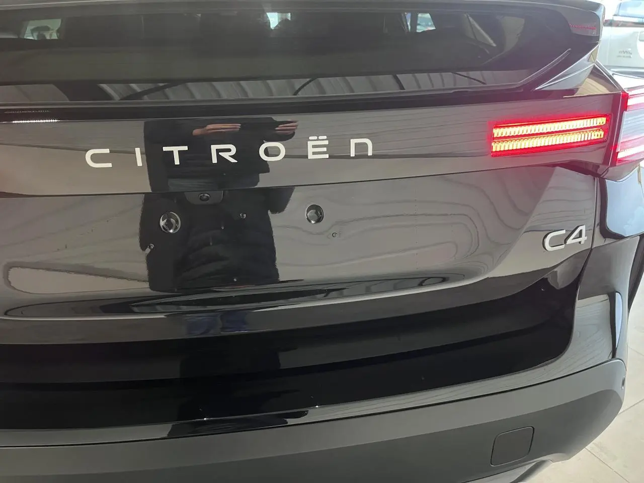 Vue arrière rapprochée du Citroën C4 noir métal avec feux arrière LED allumés et logo visible.