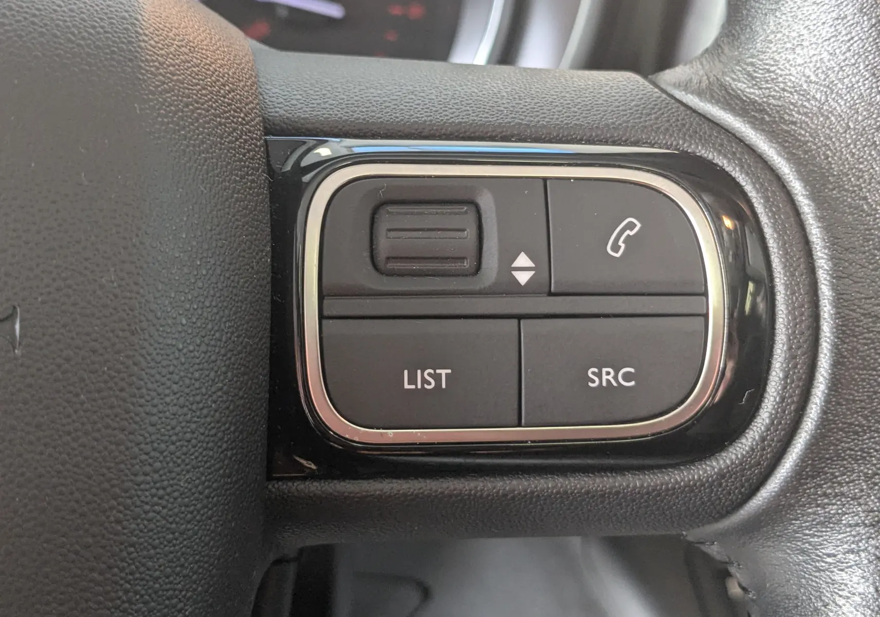 Gros plan sur les commandes multifonctions noires du volant d’un Citroën Berlingo beige, version 2019.