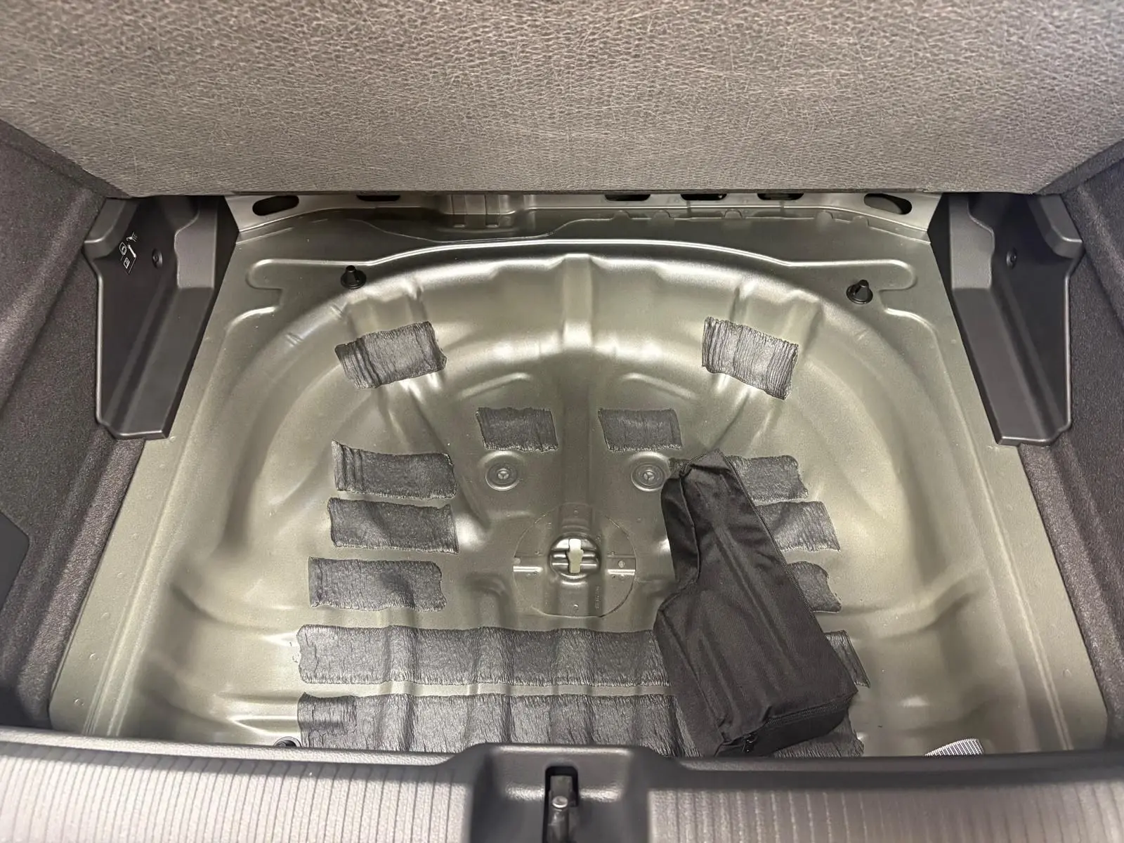 Coffre ouvert de l'Audi Q2 35 TFSI S line 2026 montrant le logement métallique de la roue de secours sans roue.