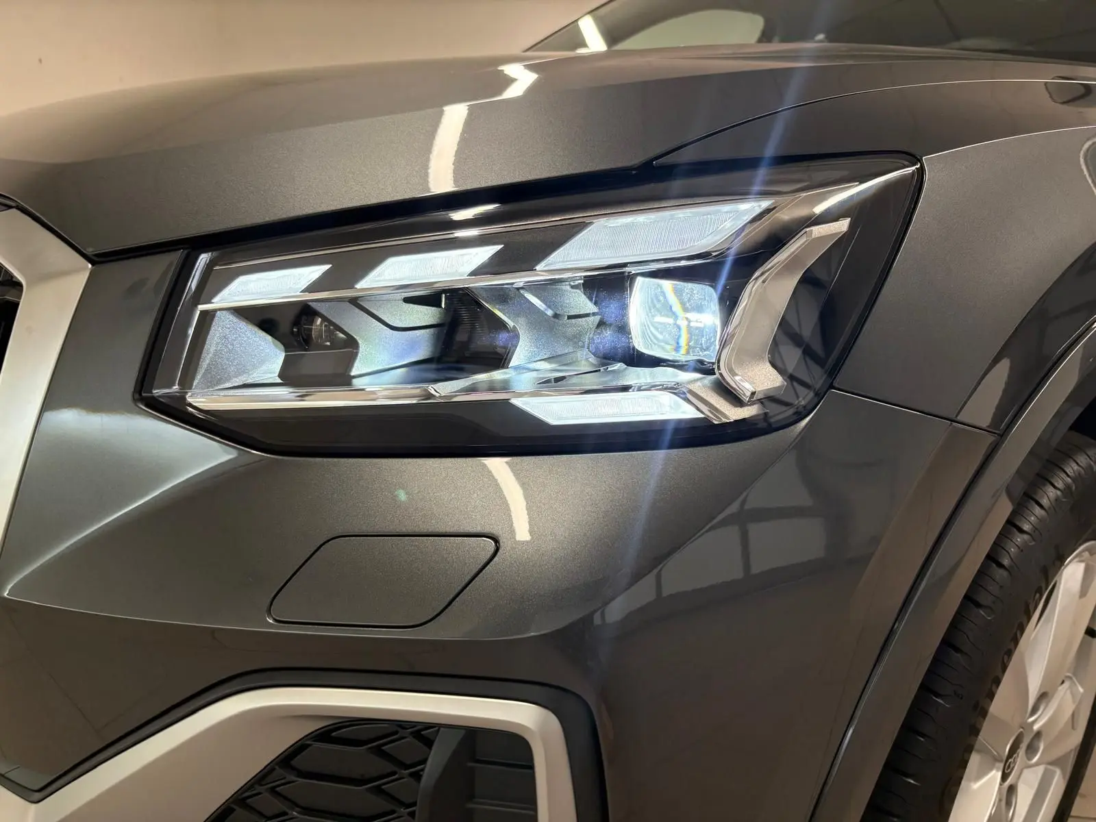 Gros plan sur le phare avant droit de l'Audi Q2 35 TFSI S Line en Gris Daytona métallisé, avec détails lumineux nets.