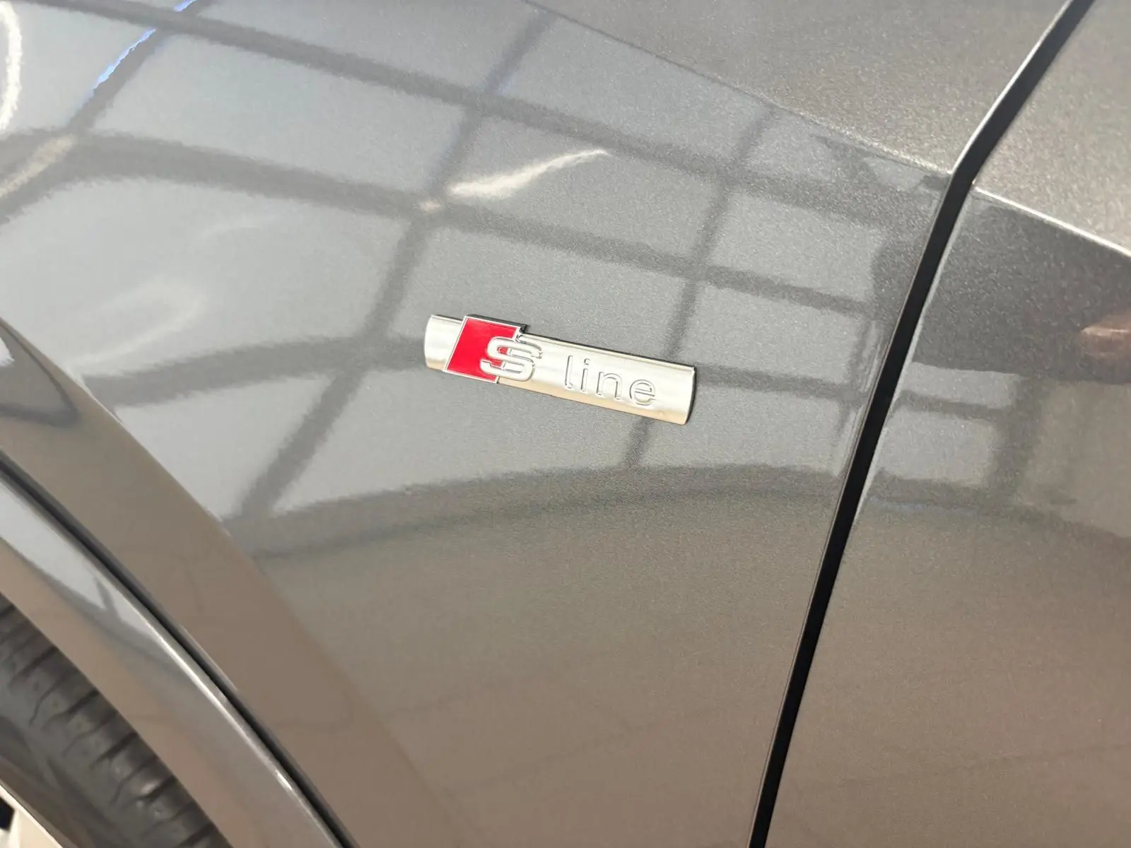 Détail du logo S line sur l’aile avant gauche d’un Audi Q2 gris Daytona métallisé, soulignant la finition sportive.