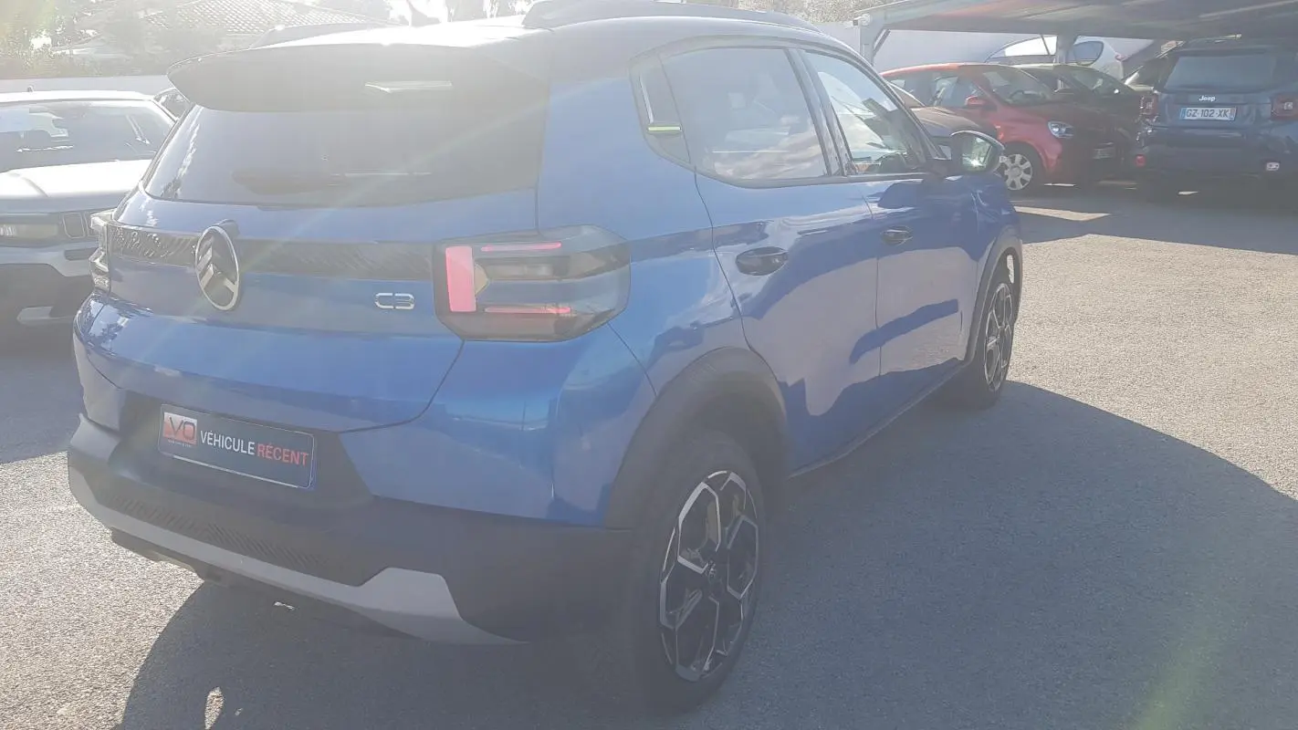 Vue 3/4 arrière droite d'une Citroën C3 bleu foncé 2024 avec jantes alliage 17 pouces et barres de toit.