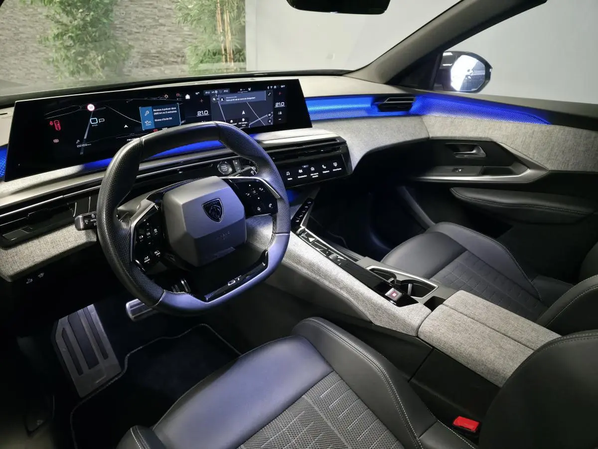 Intérieur Peugeot 3008 2025 vue côté conducteur, tableau de bord numérique panoramique et éclairage d’ambiance bleu.