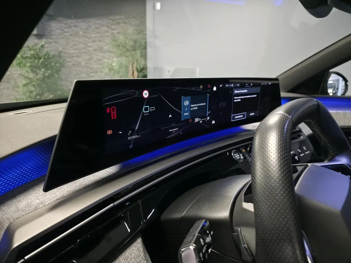Vue intérieure du tableau de bord numérique panoramique et volant perforé du Peugeot 3008 gris hybride 2025.
