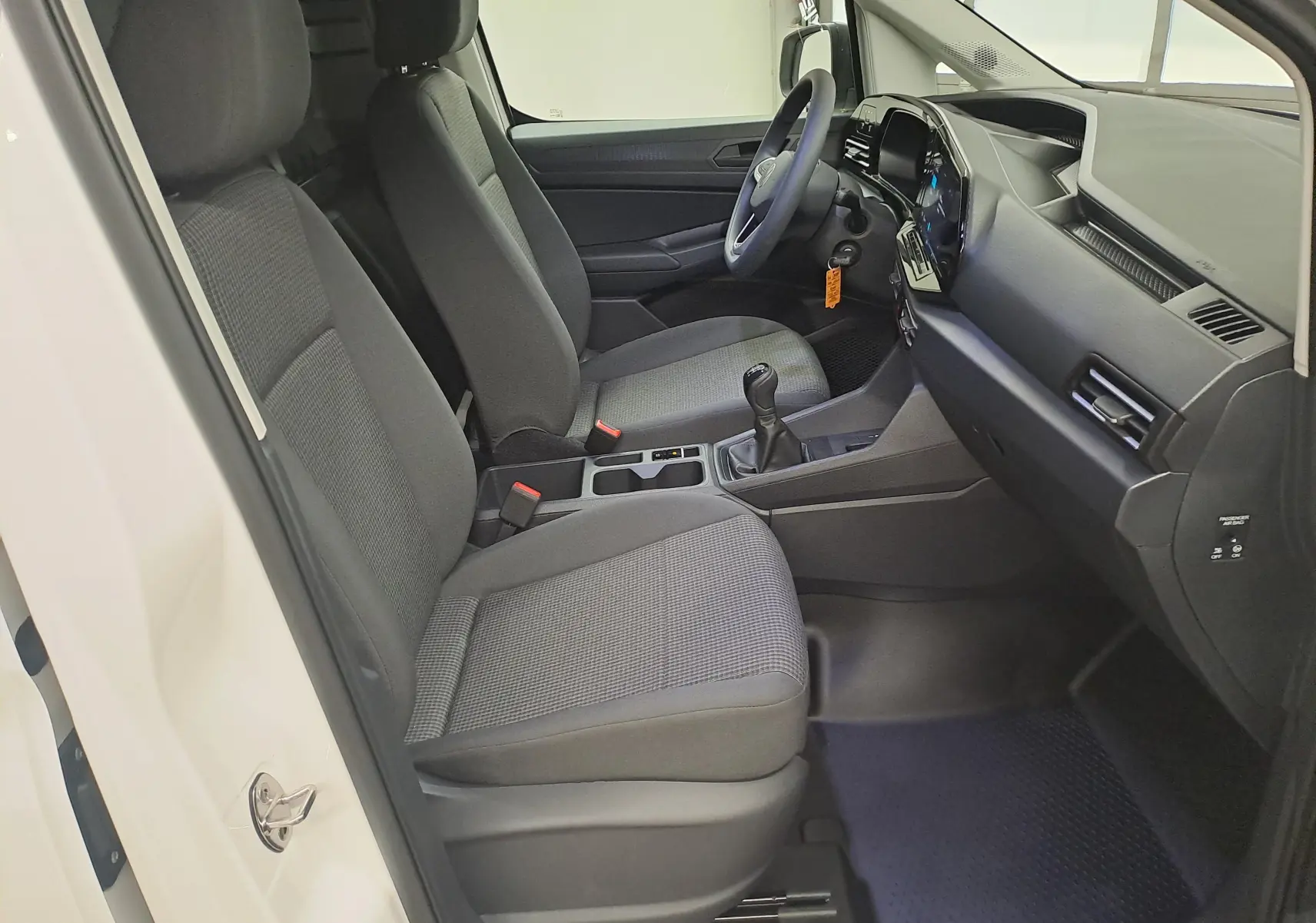 Vue intérieure côté conducteur du Volkswagen Caddy Cargo Maxi blanc Candy, avec sièges tissu gris et boîte manuelle.